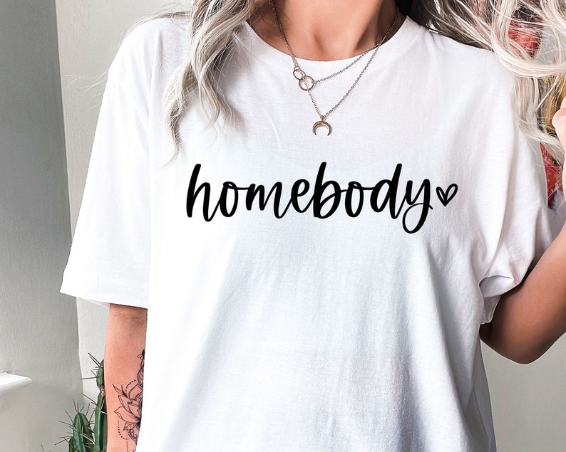 May include: White t-shirt with the text "homebody" in black cursive lettering and a small heart symbol.