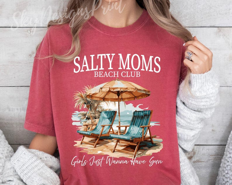 May include: Red t-shirt with the text "Salty Moms Beach Club" and a graphic of two beach chairs under a beach umbrella. The text "Girls Just Wanna Have Sun" is at the bottom of the shirt.