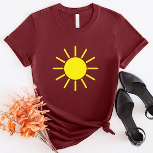 May include: A maroon t-shirt with a yellow sun graphic. The sun has a simple design with rays extending from the center.