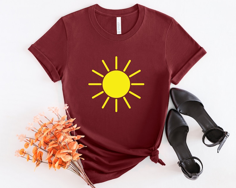 May include: A maroon t-shirt with a yellow sun graphic. The sun has a simple design with rays extending from the center.
