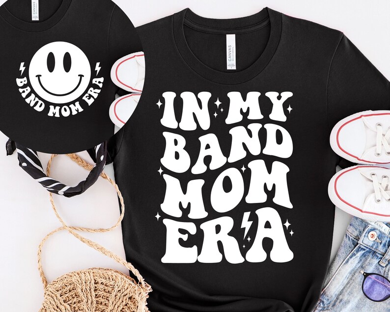 Pu&ograve; includere: Maglietta nera con testo bianco che recita "In My Band Mom Era" in un font retr&ograve;. Il testo &egrave; circondato da piccole stelle bianche e un fulmine.