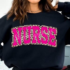 May include: Black sweatshirt with a pink "NURSE" graphic in a leopard print design.