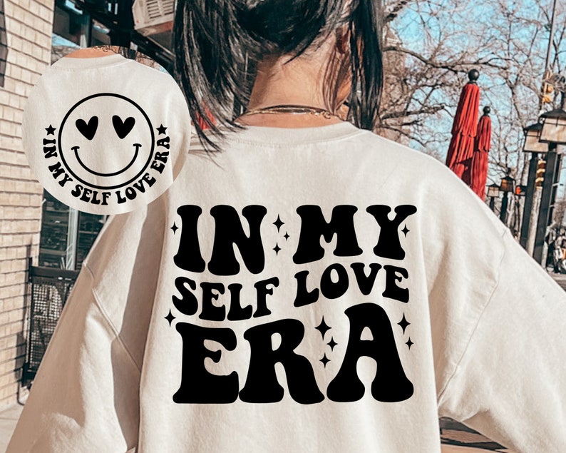 May include: White sweatshirt with black text that reads "In My Self Love Era" in a retro font. The text is surrounded by small stars.