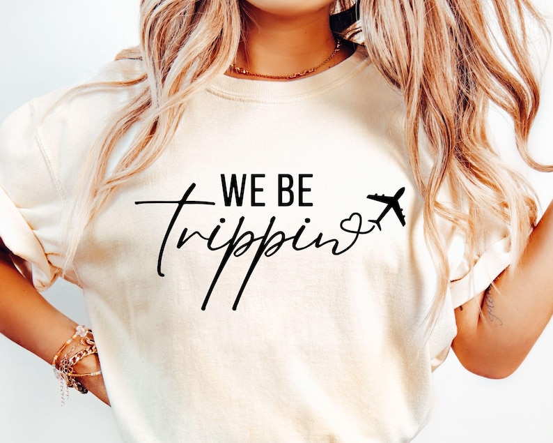 May include: White t-shirt with black text that reads "WE BE trippin'" with a small airplane and heart graphic.