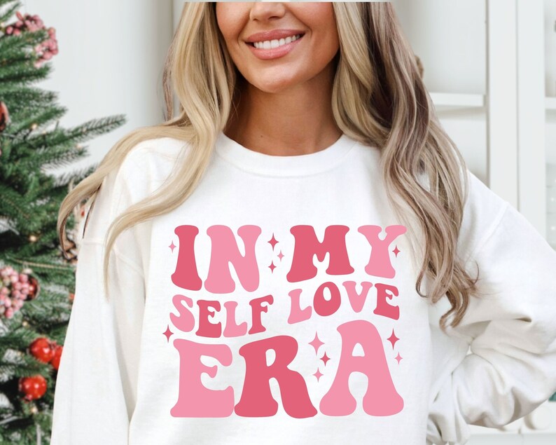 May include: White sweatshirt with pink lettering that reads "In My Self Love Era".