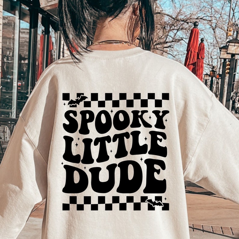 Peut inclure: Sweat-shirt cr&egrave;me avec l'inscription noire "SPOOKY LITTLE DUDE", agr&eacute;ment&eacute;e de chauves-souris et d'&eacute;toiles. Le motif comprend un motif &agrave; carreaux noir et blanc en haut et en bas. V&ecirc;tement sur le th&egrave;me d'Halloween.