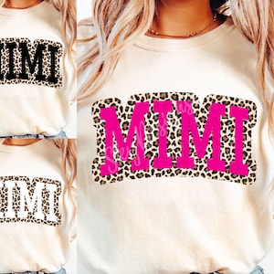 May include: A white t-shirt with a pink and brown leopard print design that says "MIMI" in large pink letters.