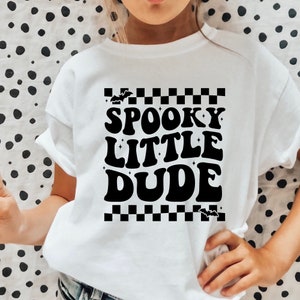 Peut inclure: T-shirt blanc avec l'inscription "SPOOKY LITTLE DUDE" en noir, dans un style r&eacute;tro. Le motif comprend des chauves-souris et un motif &agrave; carreaux, parfait pour Halloween. Le t-shirt est en mati&egrave;re souple.