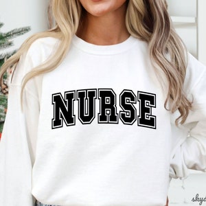 May include: White sweatshirt with black text that reads "NURSE" in a collegiate font.