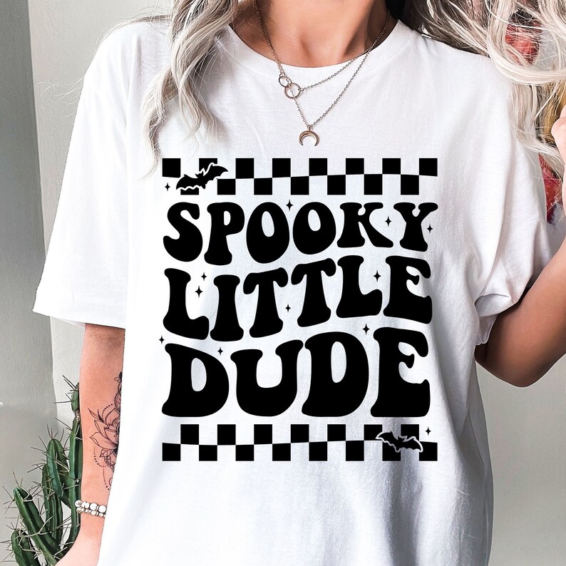 Peut inclure: T-shirt blanc avec l'inscription "SPOOKY LITTLE DUDE" en noir, dans un style r&eacute;tro. Le motif comprend une bordure &agrave; carreaux et des chauves-souris, parfait pour Halloween. Un tee-shirt d&eacute;contract&eacute;.