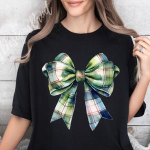 Peut inclure: T-shirt noir avec un motif de n&oelig;ud &eacute;cossais &agrave; l'aquarelle dans les tons de vert, bleu et rose. Le n&oelig;ud est le point central, avec des ombrages d&eacute;taill&eacute;s et un aspect r&eacute;aliste. Le t-shirt a un col rond classique et des manches courtes.
