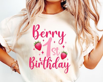 May include: A white t-shirt with pink text that reads "Berry 1st Birthday" with a pink number one and strawberry graphics.