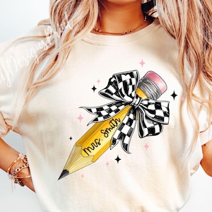 Puede incluir: Una camiseta blanca con un l&aacute;piz amarillo con un lazo a cuadros blanco y negro. El l&aacute;piz tiene el texto "Mrs. Smith" escrito en &eacute;l.