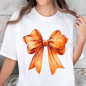 Pode incluir: Uma camiseta branca com um grande la&ccedil;o laranja estampado na frente.