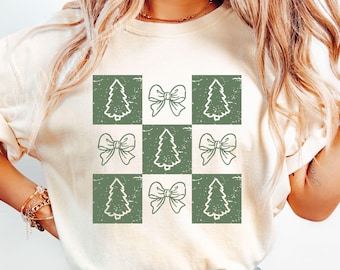 May include: A white t-shirt with a green checkered pattern featuring alternating images of Christmas trees and bows.