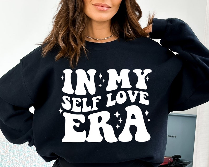 May include: Black sweatshirt with white text that reads "IN MY SELF LOVE ERA" with small white stars around the text.