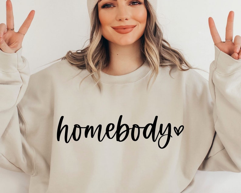 May include: A light beige sweatshirt with the text "homebody" in black cursive lettering and a small black heart.