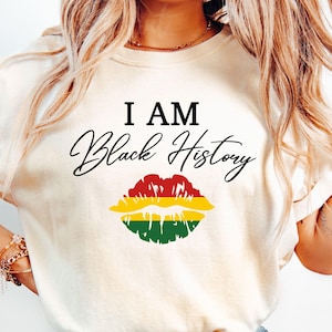 Puede incluir: Una camiseta blanca con el texto "I AM Black History" en letras negras y una impresión de labios rojo, amarillo y verde.