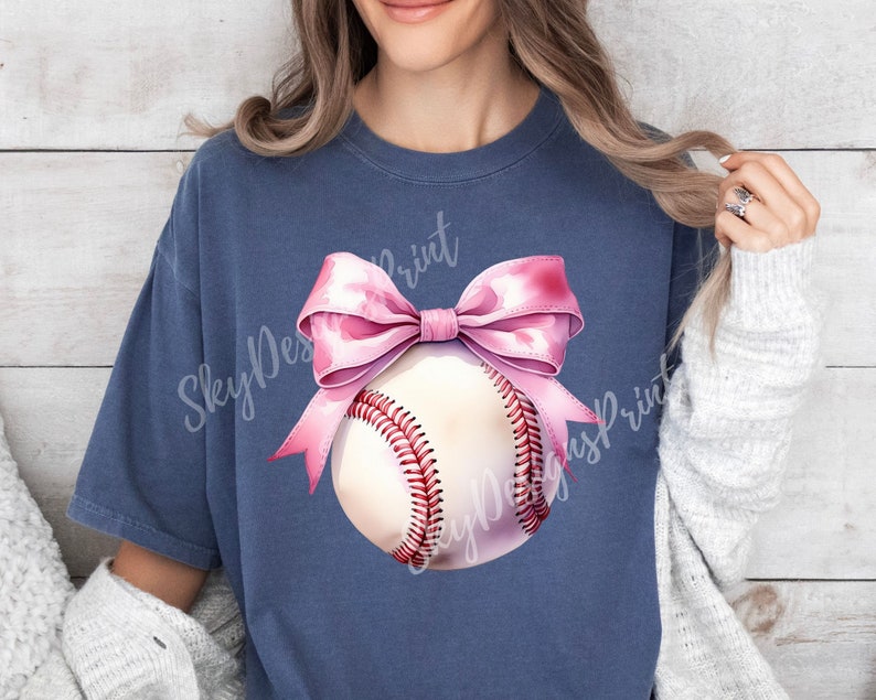 May include: A navy blue t-shirt with a pink bow and a white baseball with red stitching. The text "Sky Designs Print" is visible on the shirt.