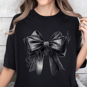 May include: A black t-shirt with a large, gray and black bow design. The bow is centered on the shirt and is the main focus of the design.