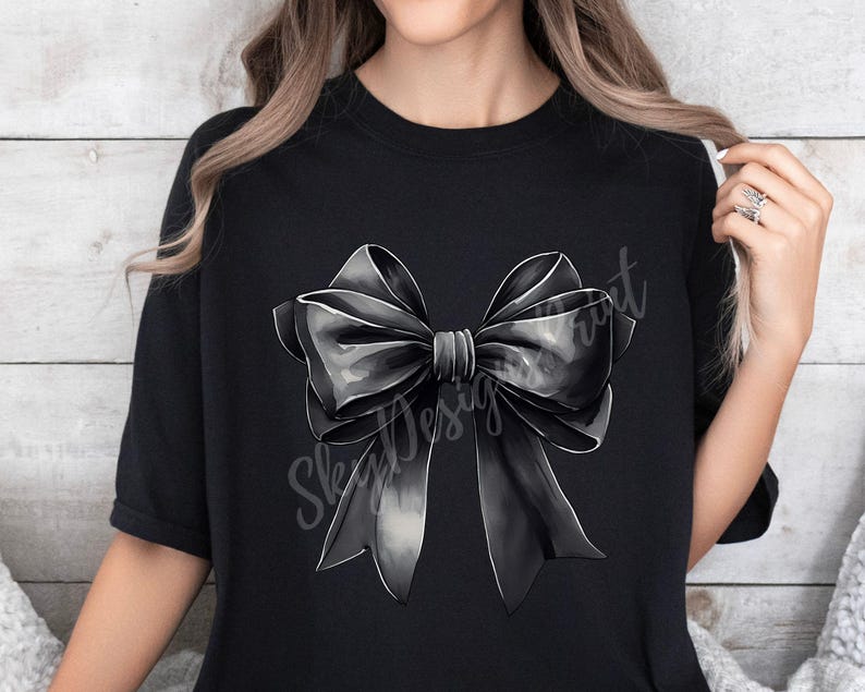 May include: A black t-shirt with a large, gray and black bow design. The bow is centered on the shirt and is the main focus of the design.