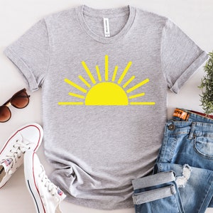 May include: A gray t-shirt with a yellow sun graphic. The sun has a simple design with rays extending from the center.