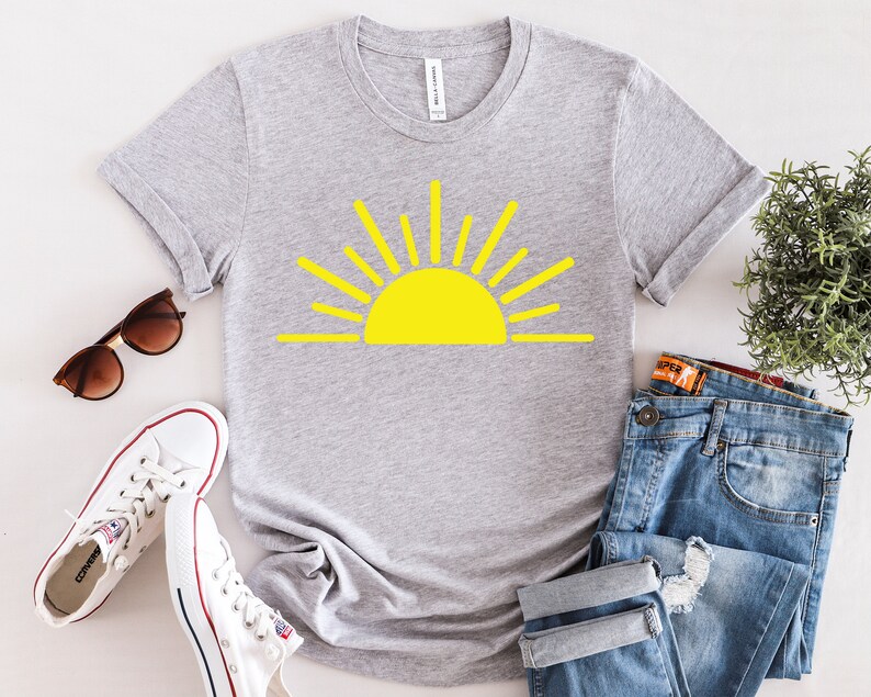 May include: A gray t-shirt with a yellow sun graphic. The sun has a simple design with rays extending from the center.