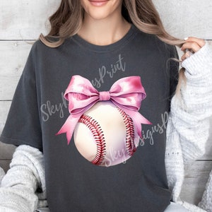 May include: A gray t-shirt with a pink bow and a white baseball with red stitching. The text "Skyline Print" and "Skyline Designs" is visible on the shirt.