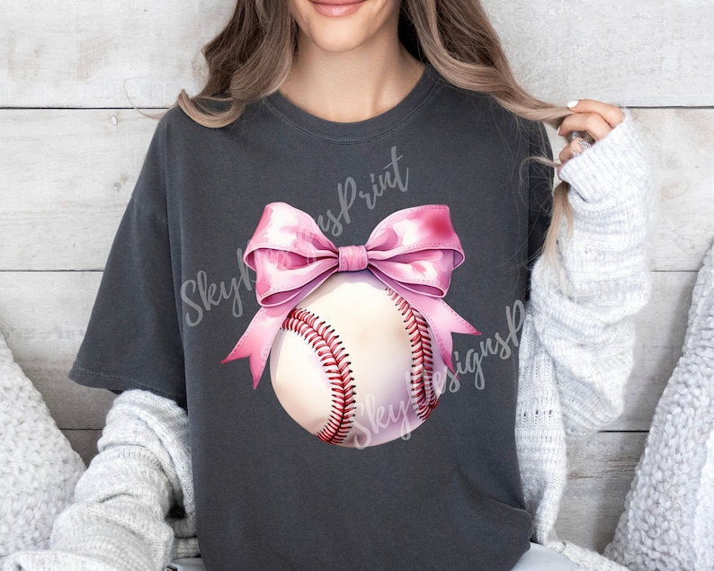 May include: A gray t-shirt with a pink bow and a white baseball with red stitching. The text "Skyline Print" and "Skyline Designs" is visible on the shirt.