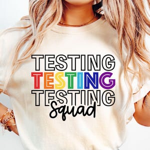 May include: A white t-shirt with the text "Testing Testing Testing Squad" in rainbow colors.