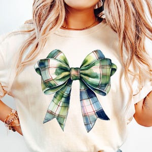 Peut inclure: T-shirt cr&egrave;me avec un grand n&oelig;ud de style aquarelle. Le n&oelig;ud pr&eacute;sente un motif &agrave; carreaux dans les tons de vert, de bleu et de blanc. Le t-shirt est de style d&eacute;contract&eacute;, adapt&eacute; au quotidien.