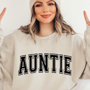 May include: A beige sweatshirt with the word "AUNTIE" printed in black block letters.