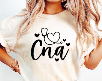May include: A white t-shirt with a black graphic design featuring a stethoscope, a heart, and the word "CNA".