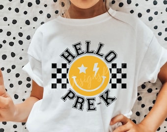 May include: White t-shirt with black text that says "Hello Pre-K" and a yellow smiley face with a lightning bolt and stars. The smiley face is surrounded by a black and white checkered pattern.
