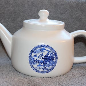 May include: White ceramic teapot with a blue and white circular design. The teapot has a curved spout, a rounded handle, and a lid with a small knob. The blue design features a landscape scene.