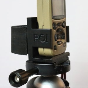 May include: A black plastic tripod mount with a strap and the word "POI" printed on it. A beige handheld device with a screen and buttons is attached to the mount.