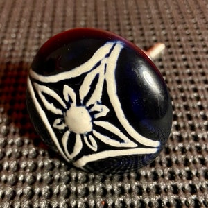 May include: A blue ceramic cabinet knob with a white floral design. The knob has a shiny finish and a simple, elegant style.