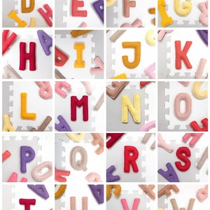 Op de afbeelding: Een set kleurrijke gehaakte alfabetletters op een witte achtergrond. De letters zijn gerangschikt in rijen en kolommen, met elke letter in zijn eigen vierkant. De letters zijn gemaakt van verschillende kleuren, waaronder rood, geel, roze, paars en bruin.