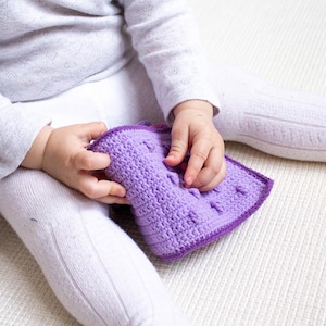 Baby exploring a crochet activity book designed from a PDF pattern, promoting sensory learning and motor skills.
