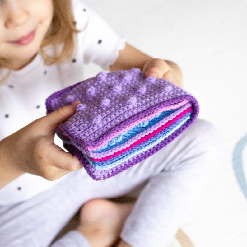 Child holding a handmade crochet sensory book created from a detailed PDF crochet pattern, perfect for Montessori-inspired play and fine motor skill development.