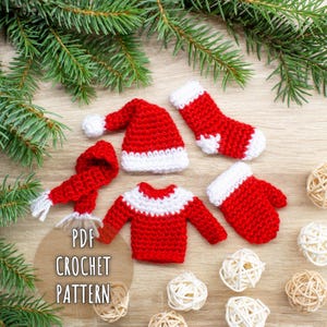 May include: A selection of red and white crocheted Christmas decorations, including a hat, scarf, sweater, stocking, and mittens. The items are displayed on a wooden surface with pine branches and decorative balls. The text "PDF CROCHET PATTERN" is visible.