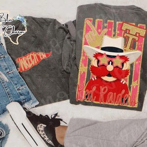May include: Two gray long-sleeved shirts. One shirt has the text "WRECK'EM" in red on a red banner. The other shirt features a cartoon character with star-shaped sunglasses and the text "Red Raiders".