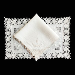 May include: A white embroidered handkerchief with a floral design and the word "Hope" in the center, folded and placed on a white crocheted lace doily.