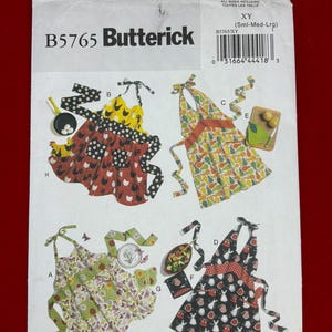 May include: A Butterick B5765 sewing pattern envelope featuring illustrations of four different apron styles. The designs include various patterns such as chickens, pears, butterflies, and kitchen utensils, with tie-neck closures and pockets.