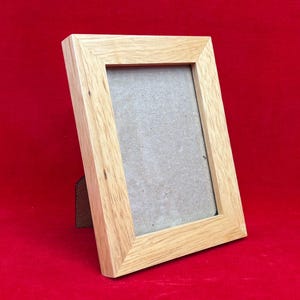 May include: A rectangular picture frame constructed from light-colored wood with a visible natural grain pattern. The frame features a mitered corner design and includes a plain, neutral-toned backing board visible within the central opening.