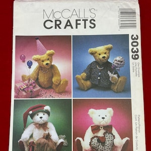 May include: A McCall's Crafts 3039 sewing pattern envelope featuring four teddy bears. The bears are shown in various outfits including a party hat, a dark patterned shirt, a red Santa hat, and a bow tie with a heart-shaped pillow accessory.