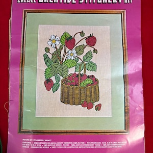 May include: A Crewel Creative Stitchery Kit featuring a strawberry basket design. The package displays a printed illustration of strawberries in a woven basket with green leaves and white flowers. It includes a 18 inch by 22 inch cut size.
