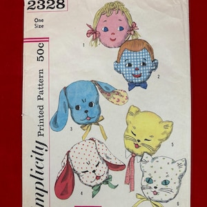 May include: A vintage Simplicity sewing pattern envelope 2328 featuring illustrations of six stuffed toy heads including two dolls, two dogs, and two cats. The envelope is white with black text and colorful drawings of the characters with bows.