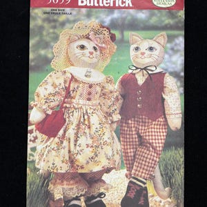May include: A Butterick sewing pattern envelope featuring two cat-shaped dolls. The female cat doll wears a floral dress, a bonnet, and carries a red purse. The male cat doll is dressed in a vest, bow tie, and checkered pants. The envelope reads "5059 Butterick".