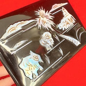 Op de afbeelding: Een rechthoekige zwarte doos met ingelegde parelmoer ontwerpen. De doos heeft een landschap met een zonnestraal, wolken en gestileerde vormen. De iriserende details cre&euml;ren een opvallend contrast met de donkere achtergrond.